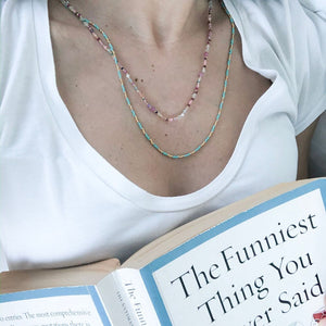 Beyaz tişörtlü kitap okuyan kadının üzerinde yeşil turkuaz doğal taşlı kolye ve renkli doğal incili doğal taşlı kolye var