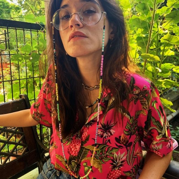 Çiçek desenli, kırmızı gömlekli kadının gözlüğünde, pembe, sarı, yeşil renkli doğal boncuklu, üzerinde Good Vibes Only" yazan uzun gözlük ipi.