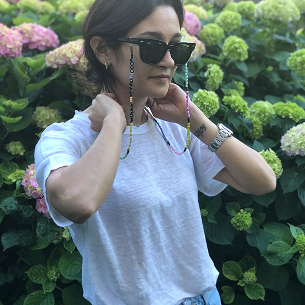 Beyaz tişörtlü kadının üzerinde, sarı, yeşil, pembe, turuncu doğal boncuklu, üzerinde Good Vibes Only yazan uzun gözlük ipi.
