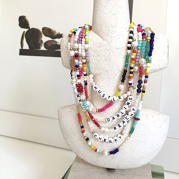 Taş mermer üzerinde, İnci, mercan, lapis lazuli, rengarenk cam boncuklardan oluşan üzerinde Beachy, Cheeky, Hustle, Darling yazılı choker kolyeler. 