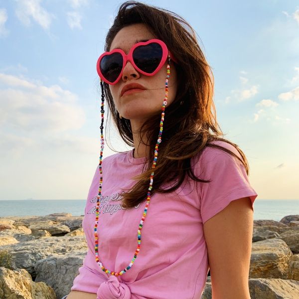 Pembe gözlük ve pembe tişörtlü kadının üzerinde Love is Love yazan, renkli boncuklu, uzun gözlük ipi.
