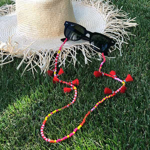 Çimin üzerinde, yanında hasır şapka bulunan, kırmızı, sarı boncuklu, üzerinde Strawberry Lemonade yazan gözlük ipi.