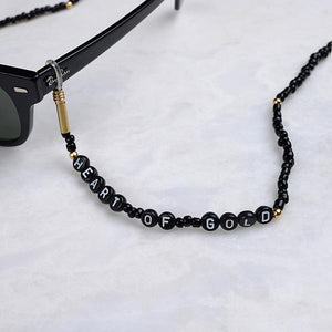 Beyaz mermer üzerinde siyah boncuklardan oluşan, silikon tutacaklı üzerinde "Heart of Gold" yazan gözlük zinciri
